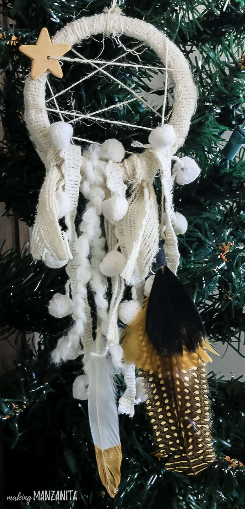 A mini dreamcatcher ornament hanging on a christmas tree branch, and hanging fabric pieces and decorative flowers.