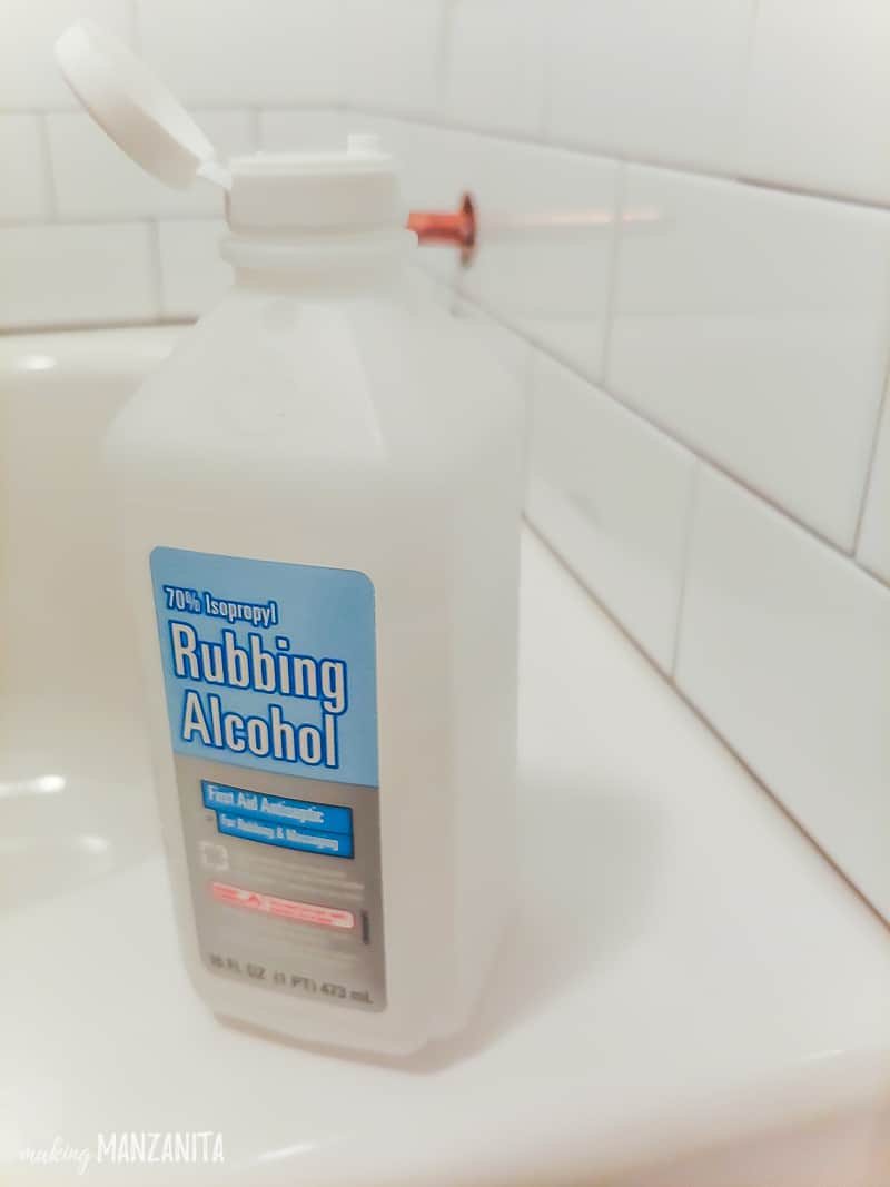 Bottle of rubbing alcohol sitting on the edge of bathtub to clean surface prior to adding shower caulk