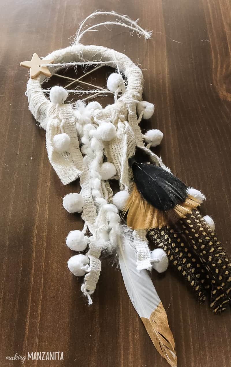 A completed mini dreamcatcher christmas ornament with hanging fabric accents, decorative feathers, a boho style star charm.