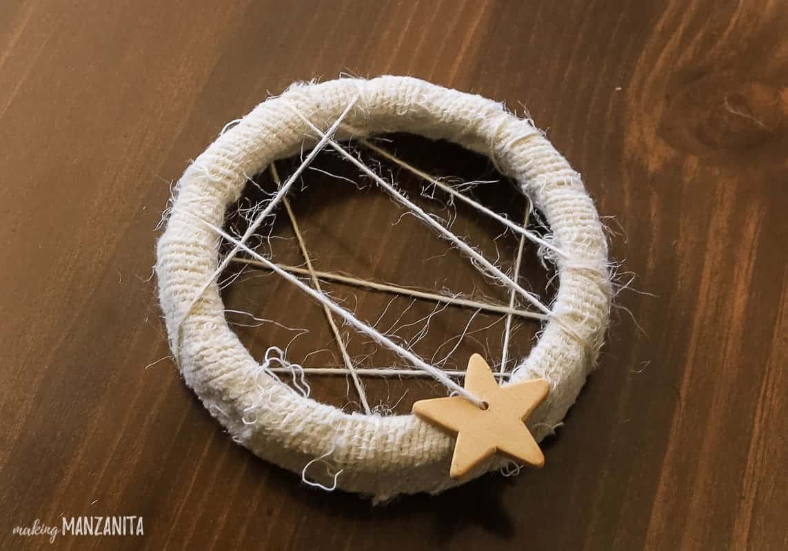A fabric-wrapped dreamcatcher ornament with a small wooden star charm attached with twine.