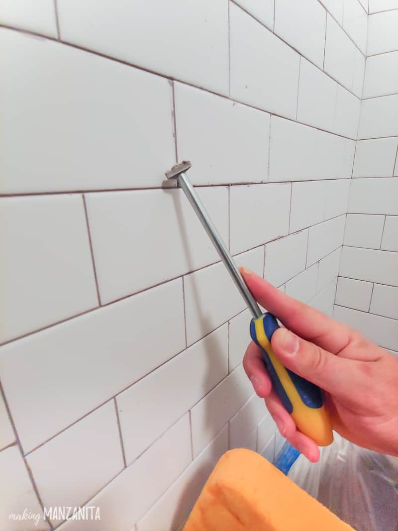 Man's hand using grout scraper tool to clean grout lines on white subway tile