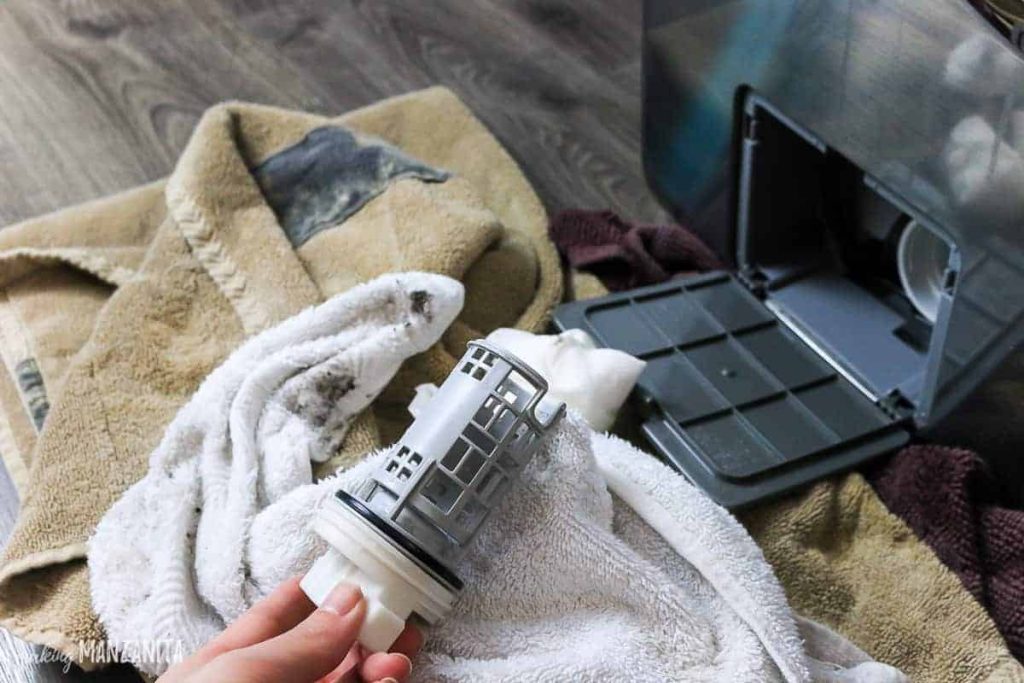 Cleaning and emptying the washer filter using a towel and rag with vinegar and water solution.