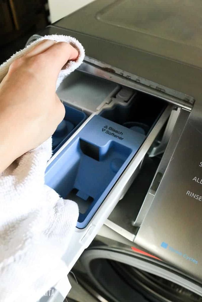 Cleaning the soap and detergent trays and drawers of the washing machine using a rag soaked in water and vinegar solution.