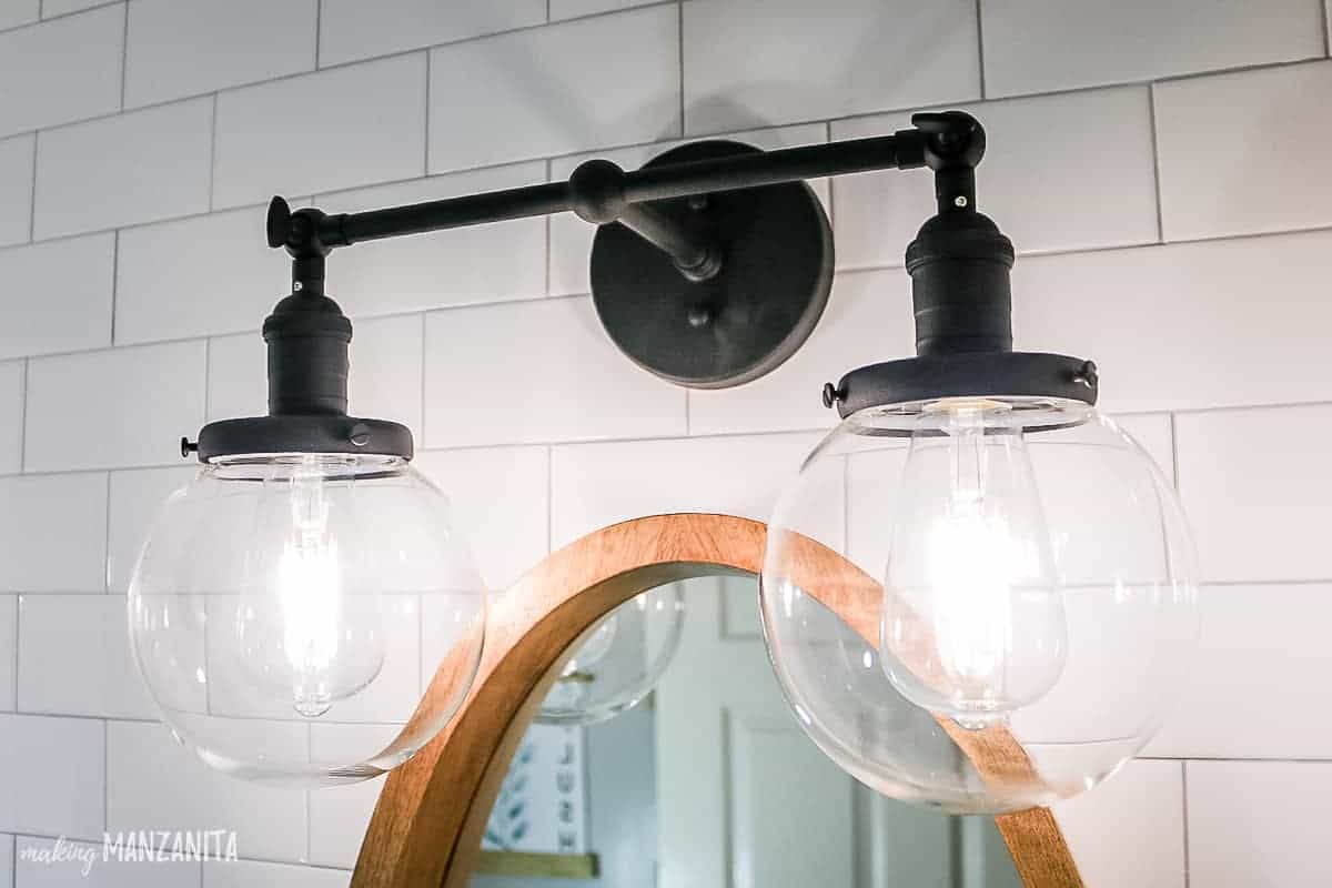 Black industrial style vanity light with 2 glass globes and daylight edison bulbs hangs over the bathroom vanity in our renovated farmhouse bathroom