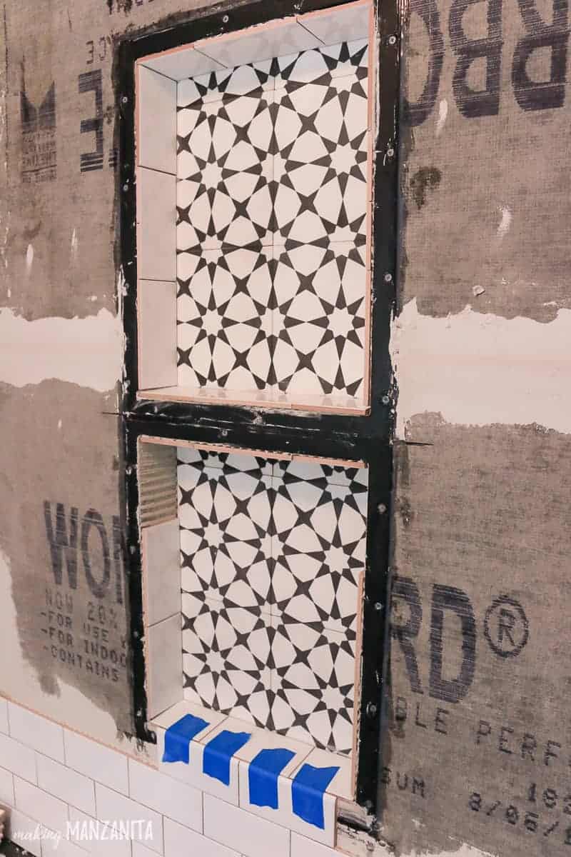 The process of tiling the installed prefab shower niche. This shower niche is being tiled with black and white geometric patterned as the background, and white subway tile on the shower niche shelves and around the border.