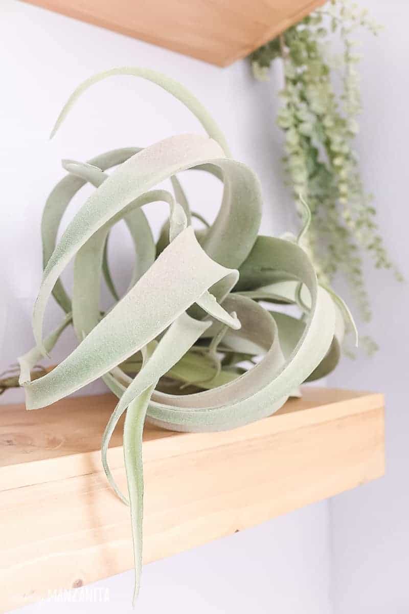 Faux airplant sitting on floating wood shelf in a boho farmhouse style bathroom