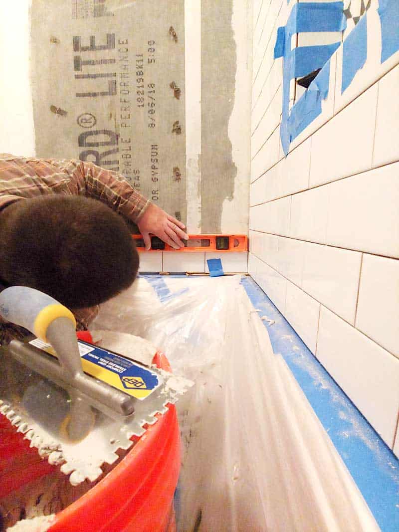Man installing subway tile walls in shower and holding a level on top making sure it is level