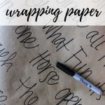 Sheet of brown shipping paper with Christmas song lyrics written on it with a Sharpie laying on top of it with text overlay that says make your own wrapping paper
