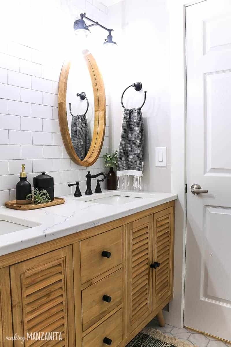 Dual sink wood vanity with shutter door fronts and slim black hardware with a white quartz countertop, white subway tile mirror and round wood mirrors in a boho farmhouse bathroom