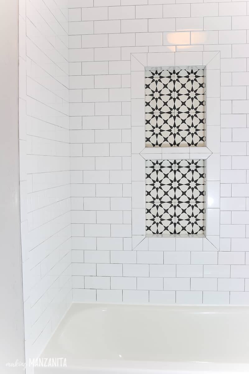 A completed installed shower niche in our bathroom shower. This prefab shower niche was tiled with black and white geometric background tile and a picture frame border created with white subway tiles. 