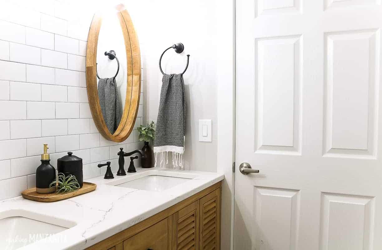 White quartz countertop that looks like marble in a modern farmhouse bathroom with white subway tile backsplash and round wood framed mirror 