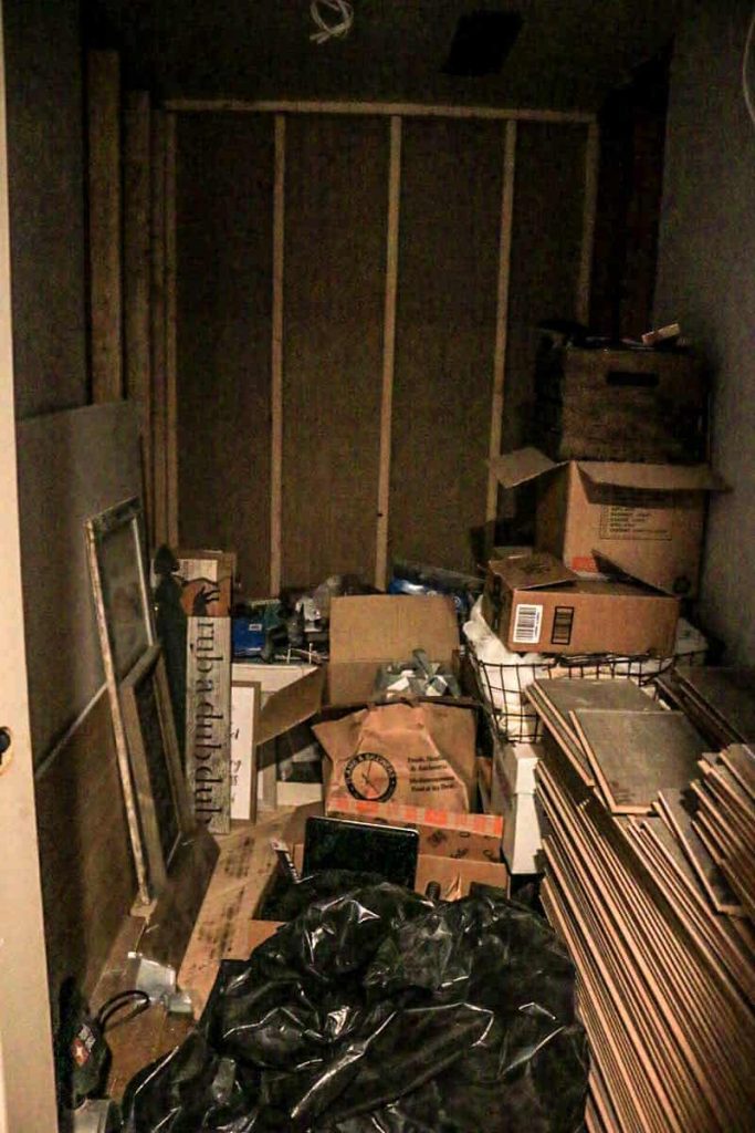 Dark skinny room filled with storage and boxes that will be converted to a boho farmhouse style bathroom