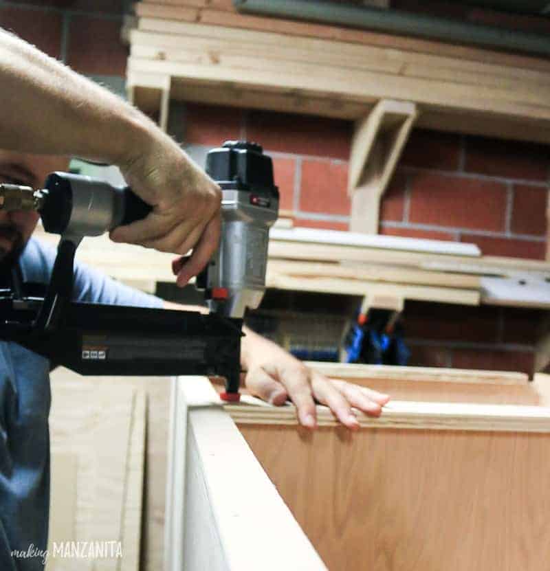 Using a nail gun to attach the front pieces of our DIY hallway storage cabinet.
