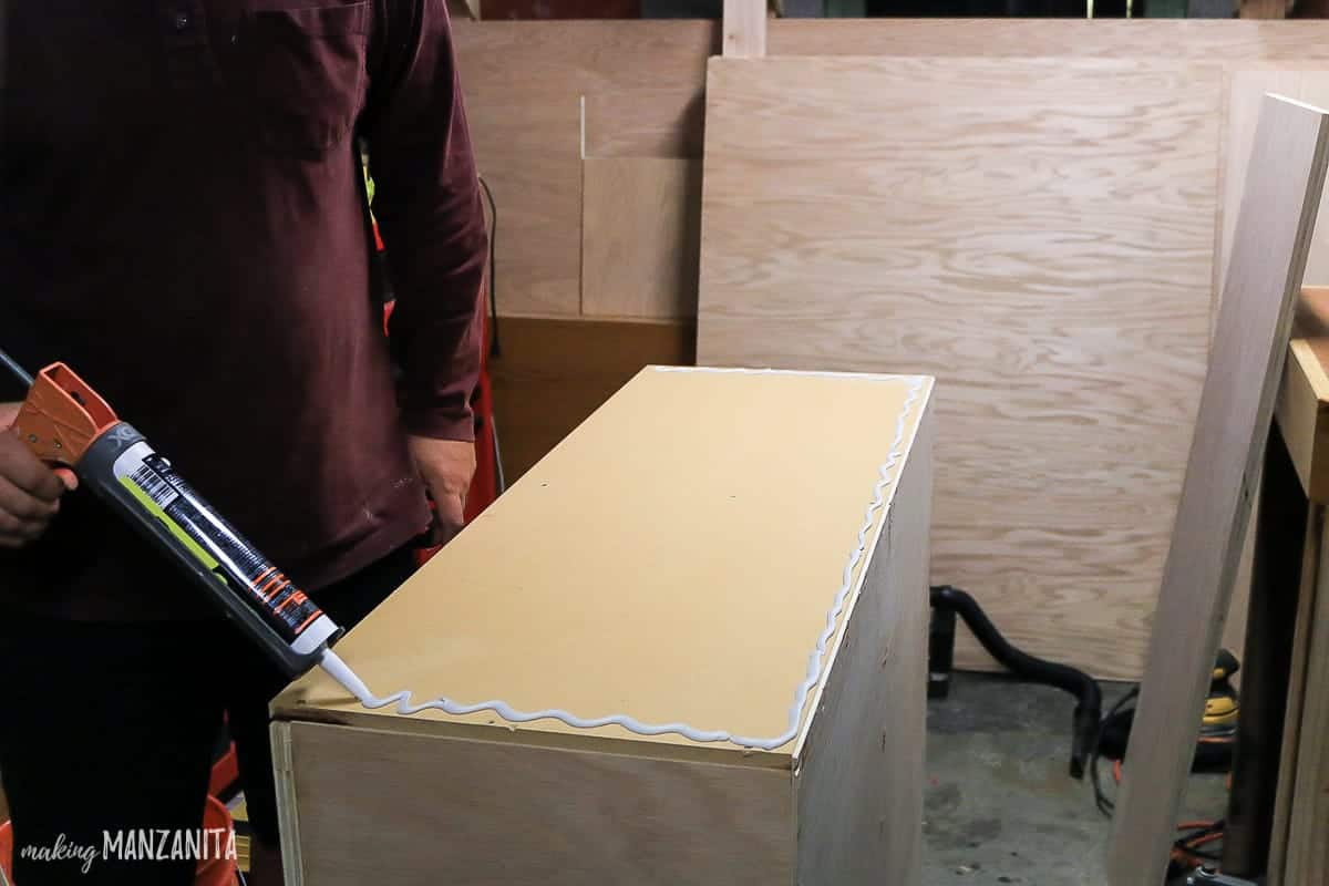 Piping construction adhesive to the top of our in-progress hallway cabinet, which will attach the cabinet countertop.