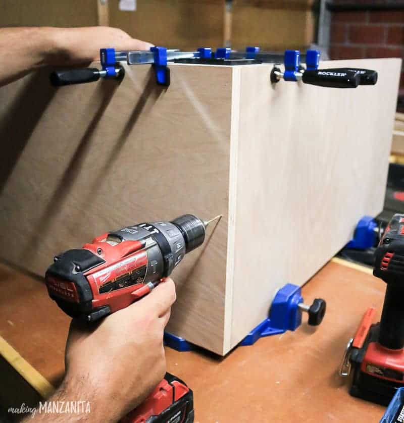 The Clamp-It Corner Clamping Jig holds together the corner of the in-progress hallway cabinet while Logan drills screws into the wood.