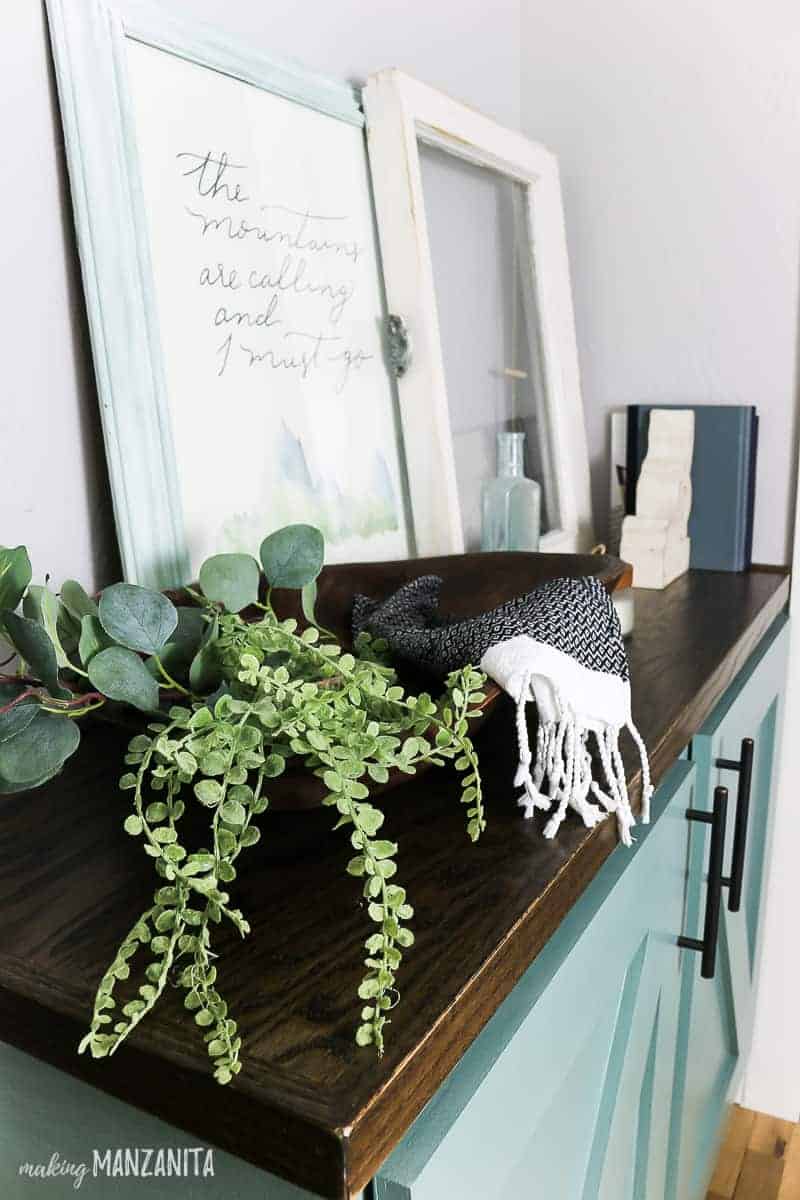Faux greenery fills a wooden accent bowl that sits atop of our new hallway storage cabinet.