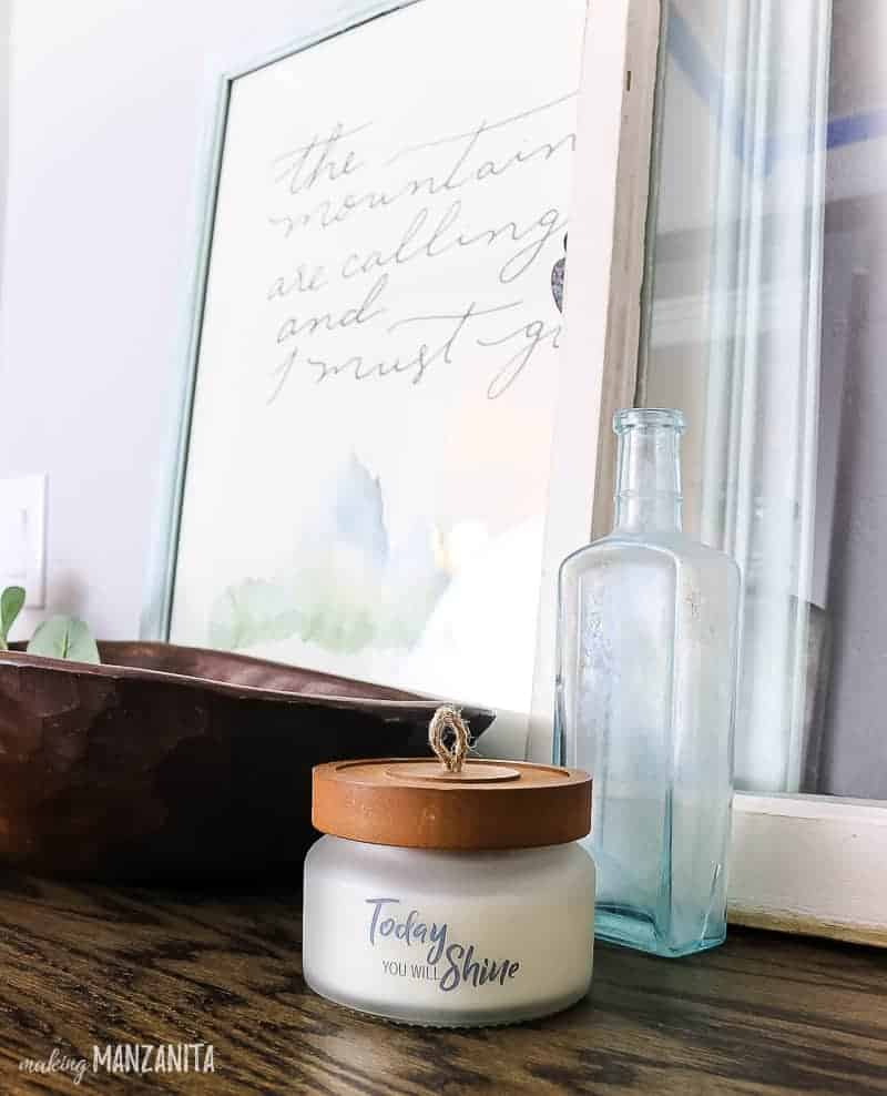 The farmhouse style decor on top of our new hallways cabinet - a small jarred candle, glass bottle, and framed print.
