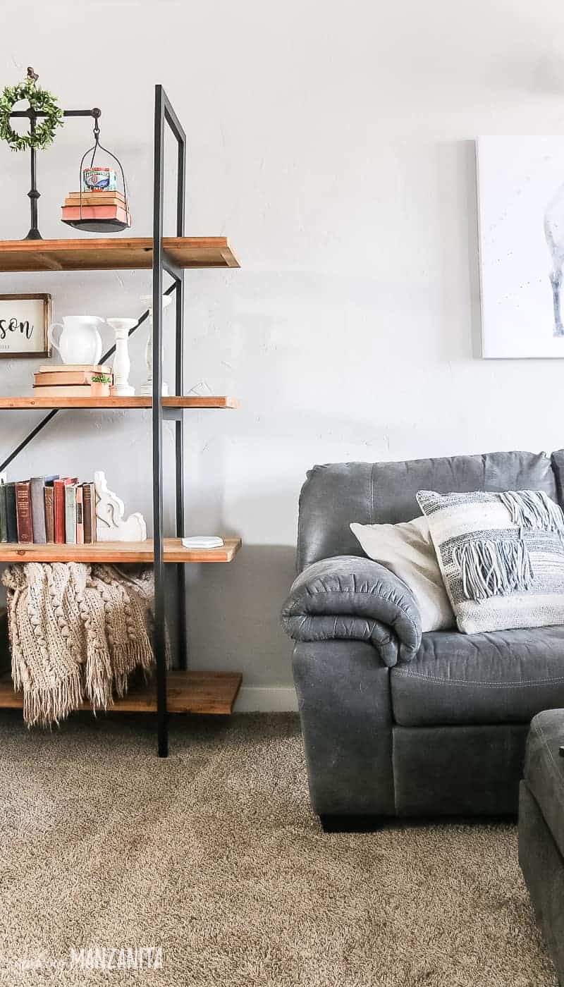 End of gray sectional couch with neutral throw pillows and corner of shelving unit decorated with modern farmhouse decor