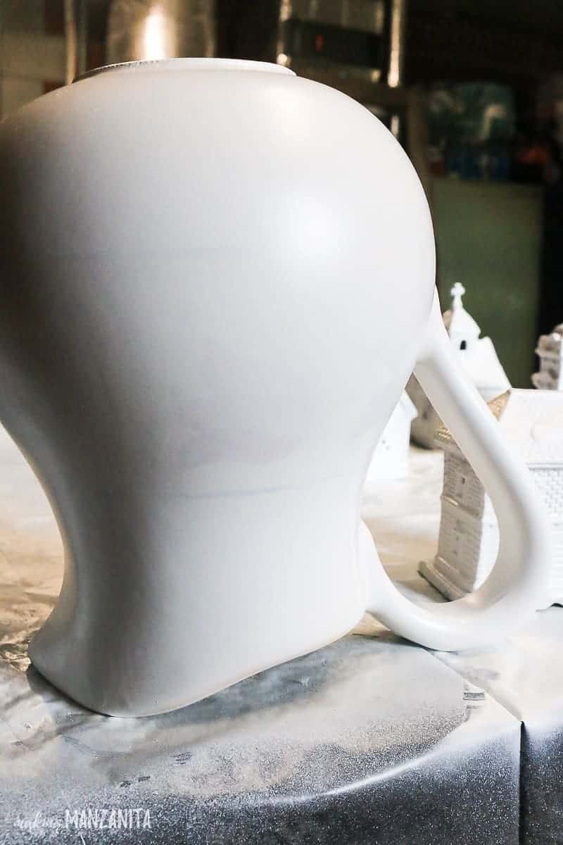 The primed and painted white ceramic pitcher sits upside down on the craft table.