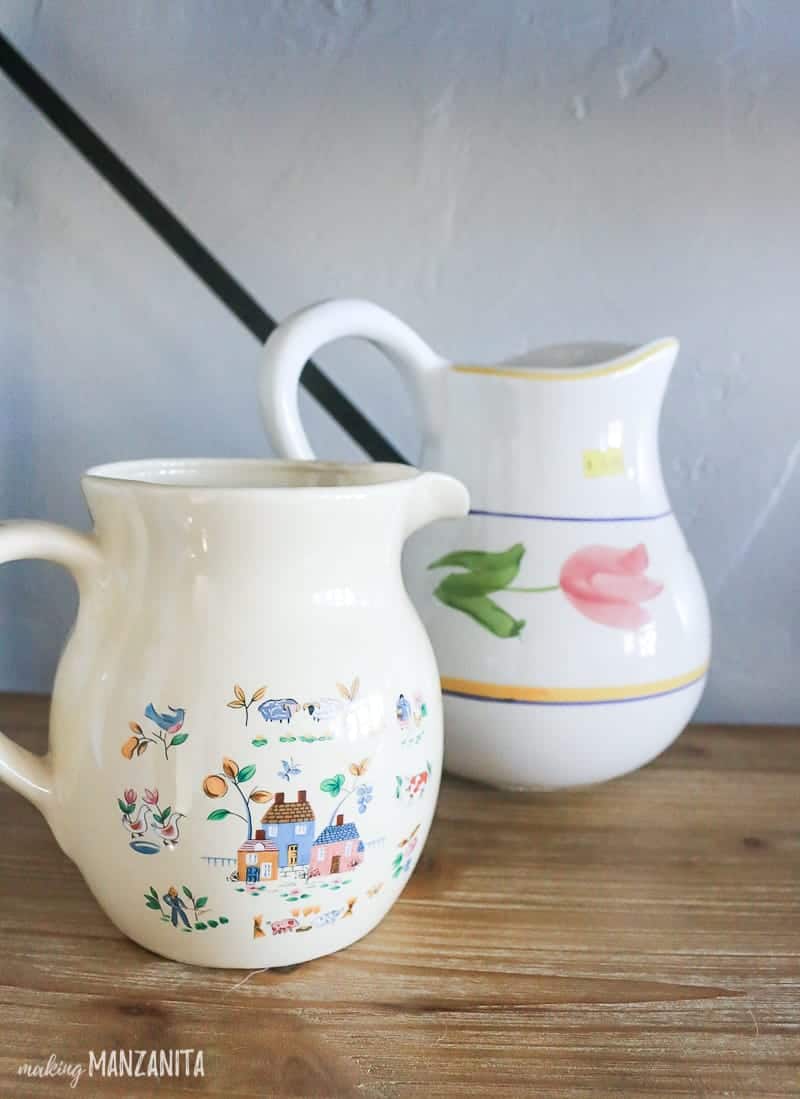 Two white ceramic thrift store pitchers with tacky designs, soon to be upcycled into white farmhouse style pitchers you can use as decor, vases, or more.