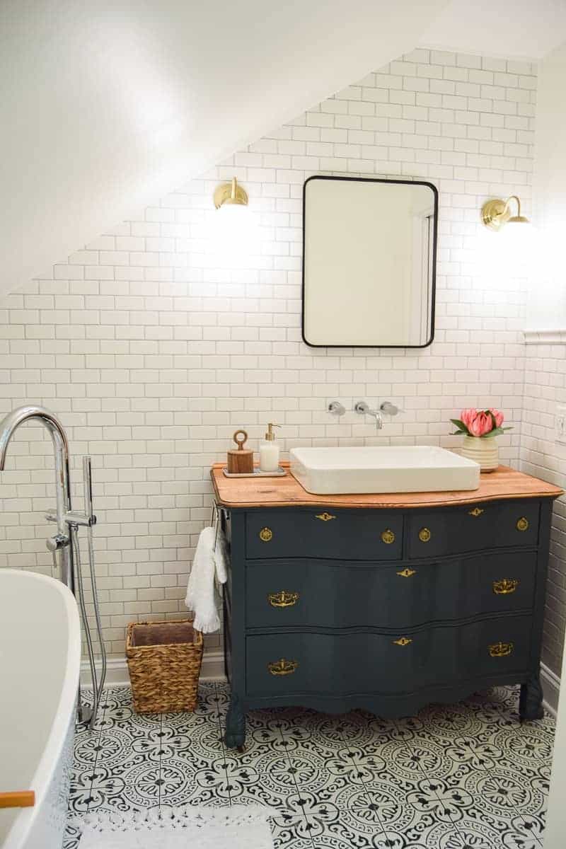 Bathroom showing blue painted vintage dresser used as vanity with a sink added, full wall of subway tile, cement tile flooring, modern globe lighting and metal framed mirror