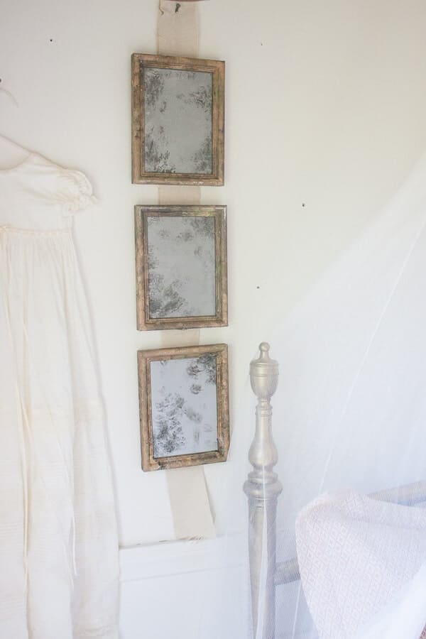 3 gold frames turned into antique looking mirrors hanging in a row in the wall with a white walls. Corner of bed frame is shown in the corner 