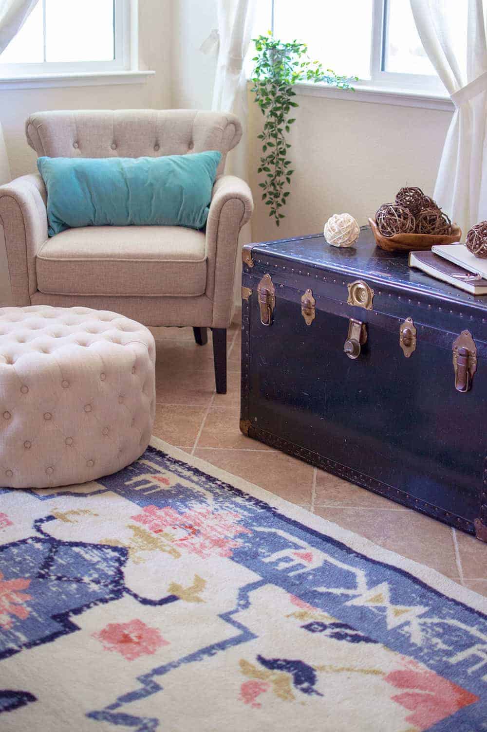 Corner of living room with vintage trunk used as side table, cream colored furniture, teal throw pillow and colorful vintage inspired rug