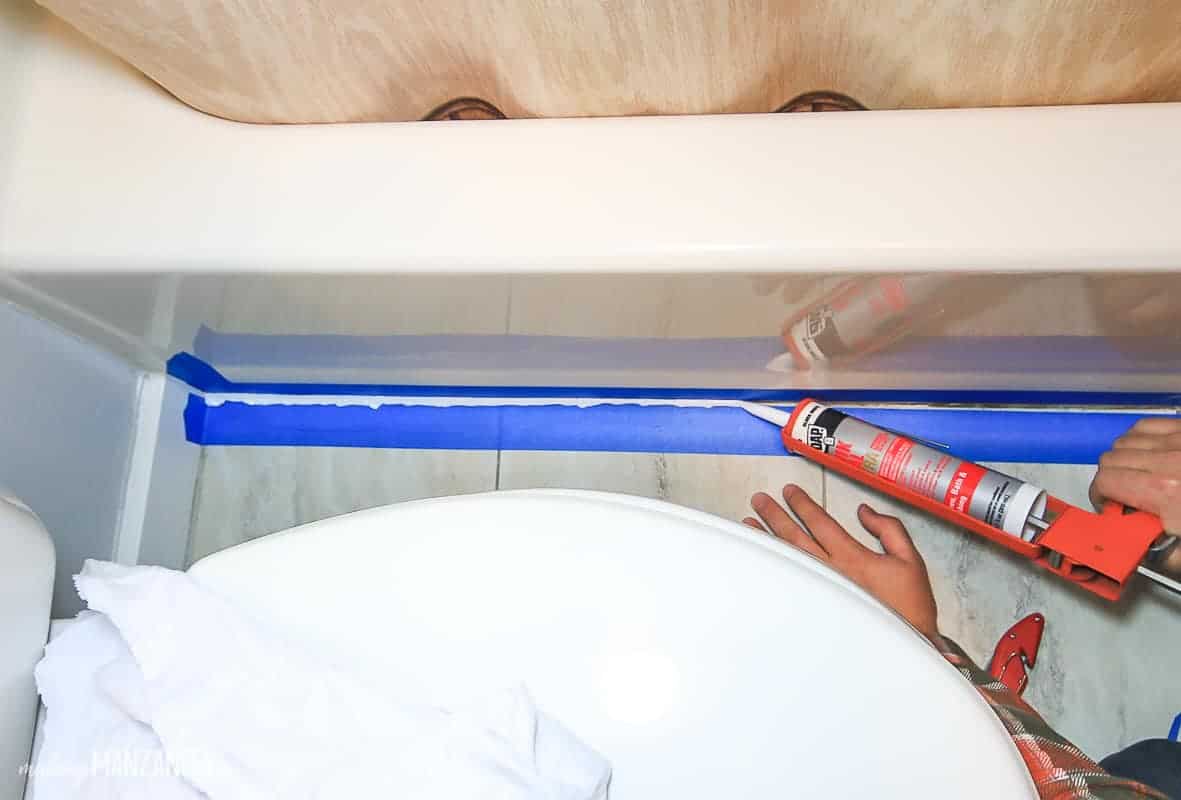 Applying a new line of caulk to the tile line where the bathtub meets the tile floor