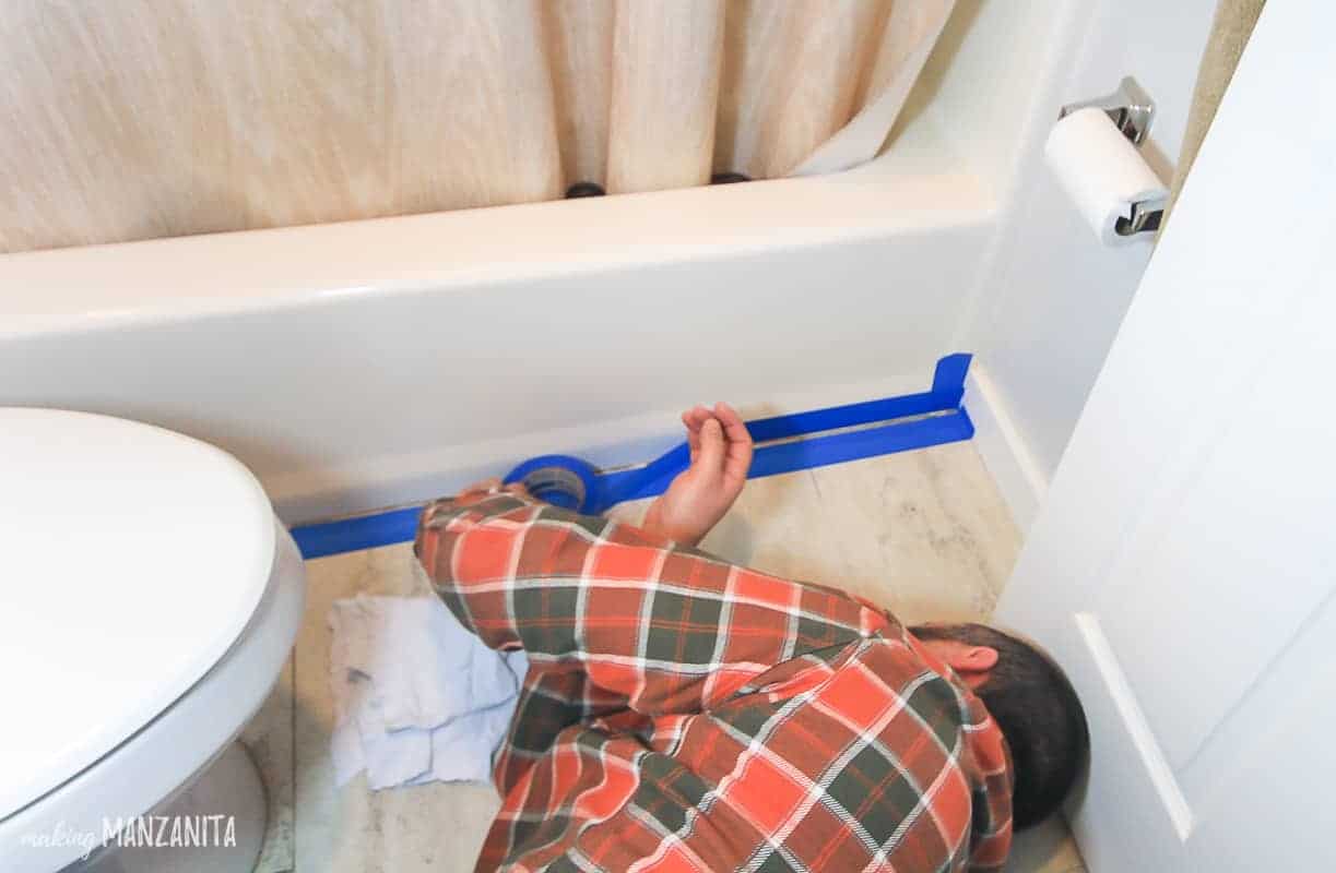 Applying painters tape to the floor and the bathtub before recaulking the bathtub