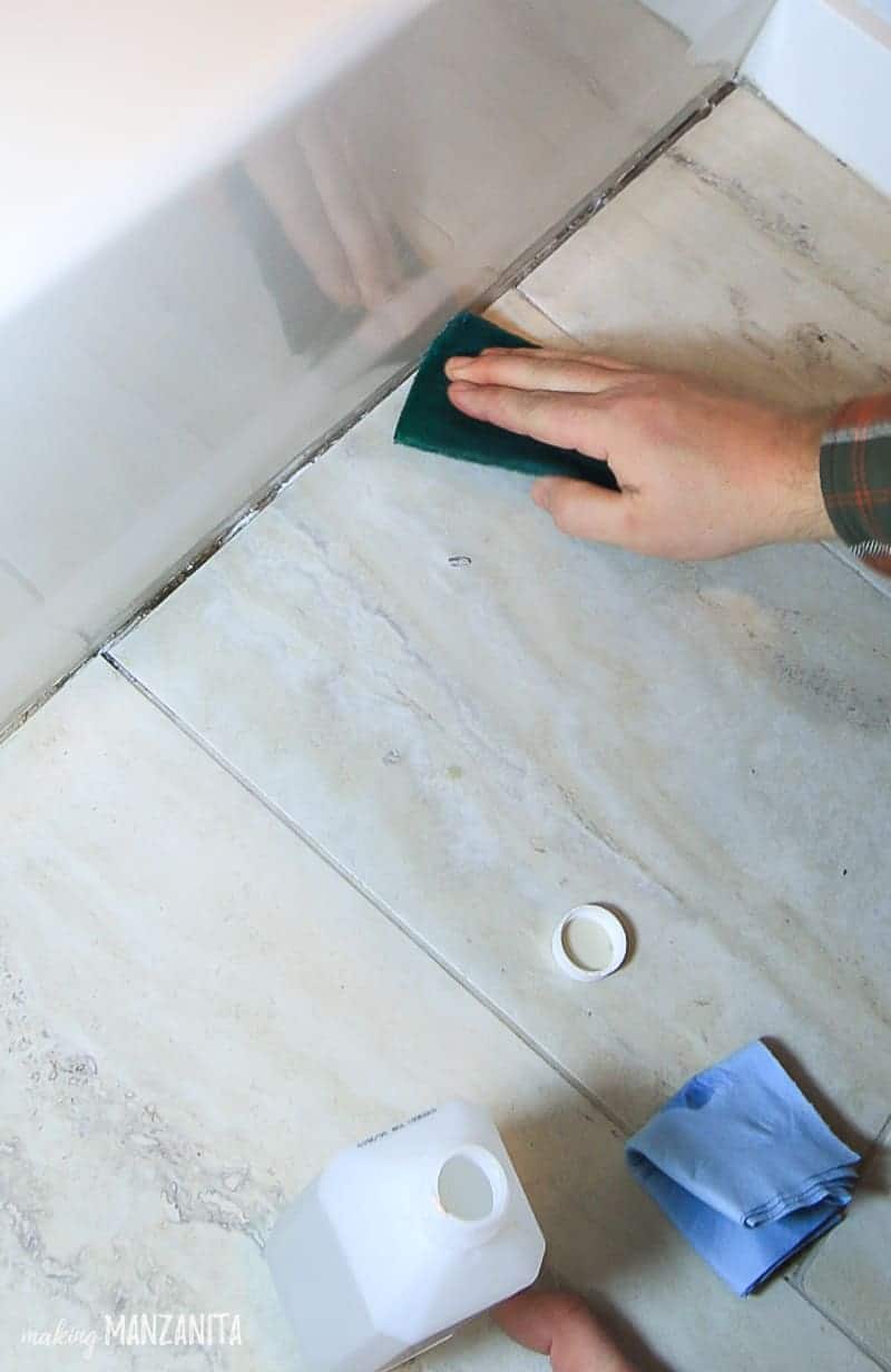 Scrubbing the caulk line with a scour pad and rubbing alcohol to remove old caulk before recaulking in bathroom