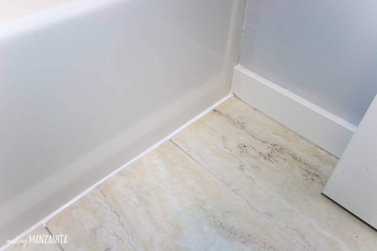 Corner of bathroom flooring and new caulk lines on bathtub