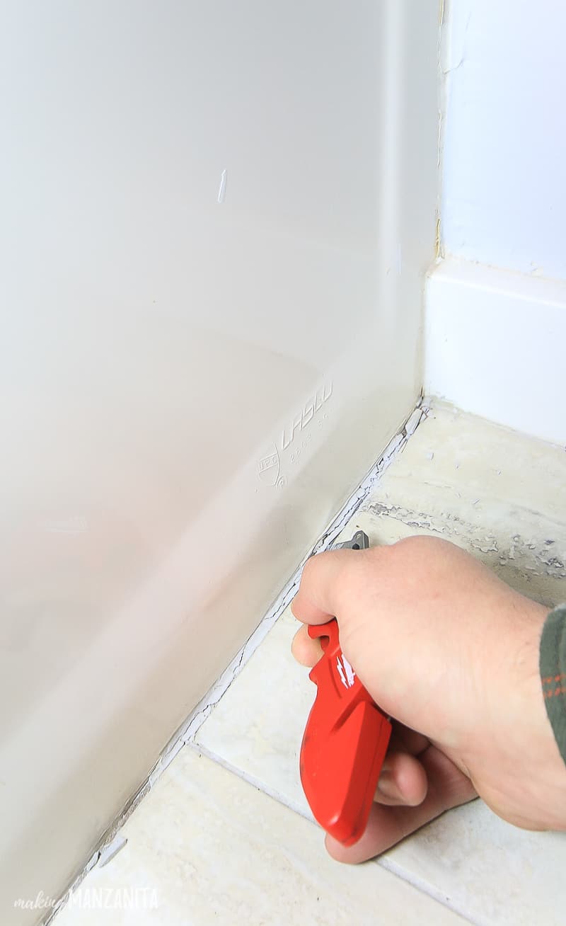 Using a utility knife to scrape old caulk off of the bathtub before recaulking the bathtub tile line