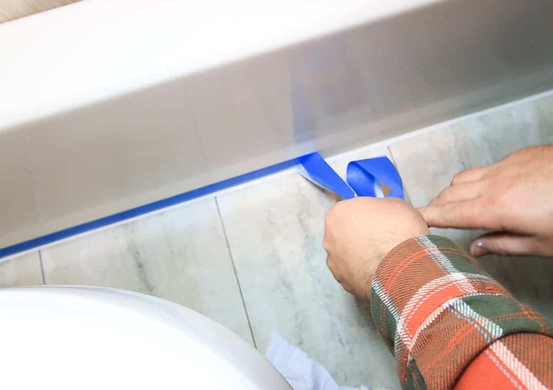 removing painter's tape from bathroom after applying new white caulk at the base of the bath tub