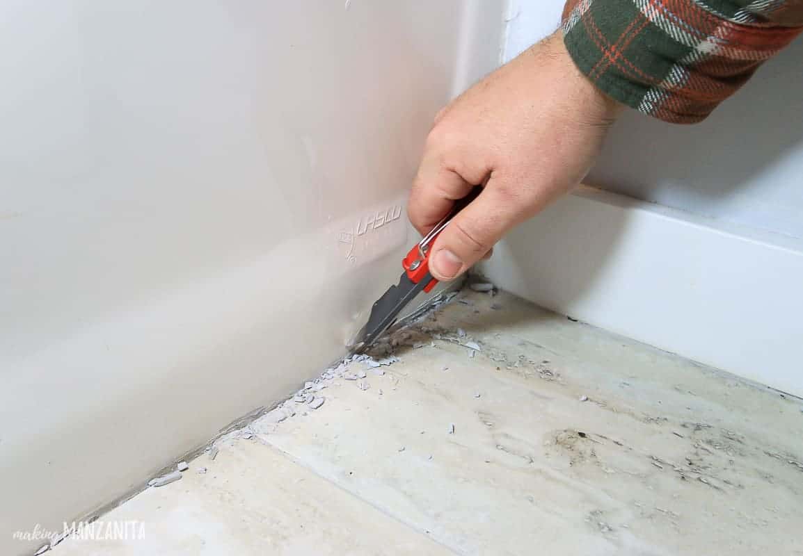 Removing old caulk in bathroom with a razor blade before recaulking 