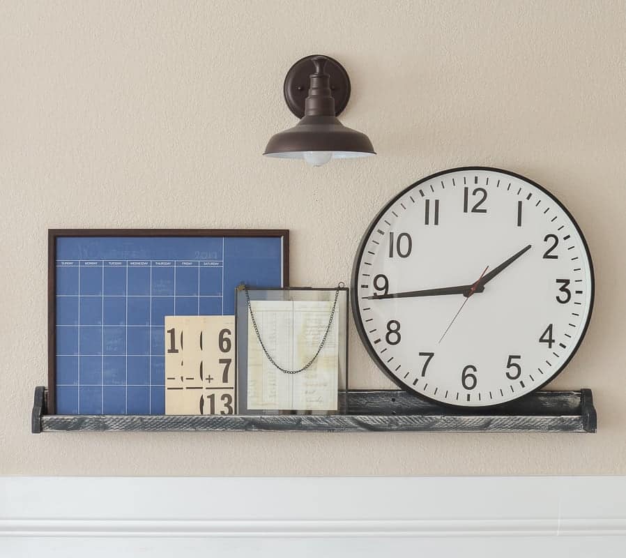 Small picture ledge shelf decorated with large clock, vintage styled framed art, math cards and an industrial sconce light