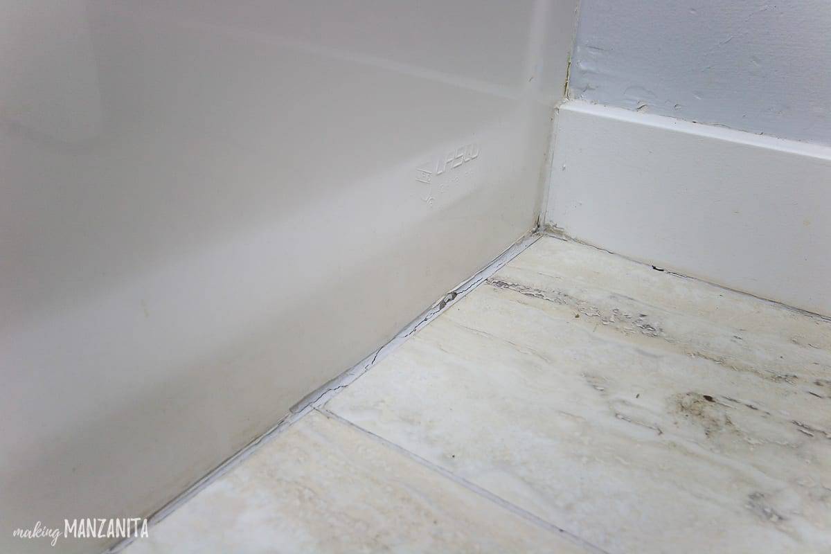 Close up shot of a caulk line at the base of a bath tub where the flooring meets the tub that dirty and cracked and needs replacing