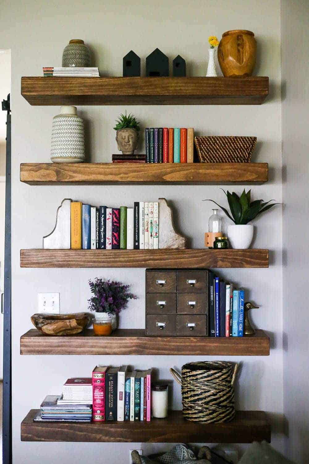 Chunky wood floating shelves in living room decorated with plants, vases, colorful books and baskets