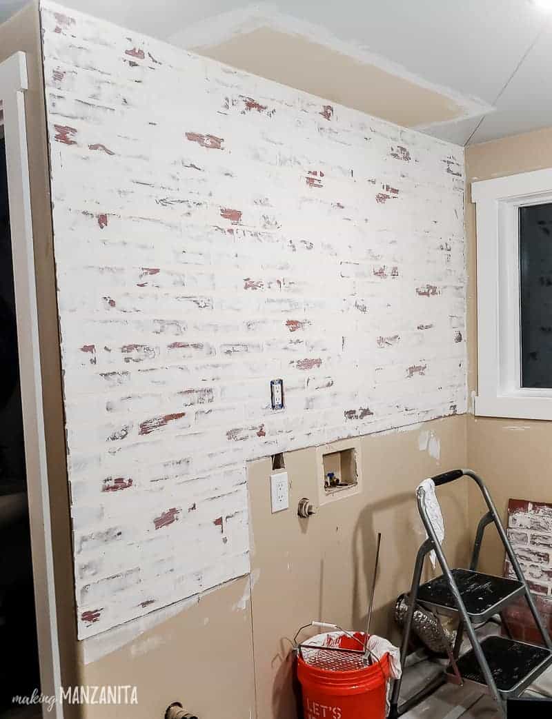 Faux brick wall in progress during laundry room renovations getting a german schmear treatment with a step stool in front of it and a bucket of water.