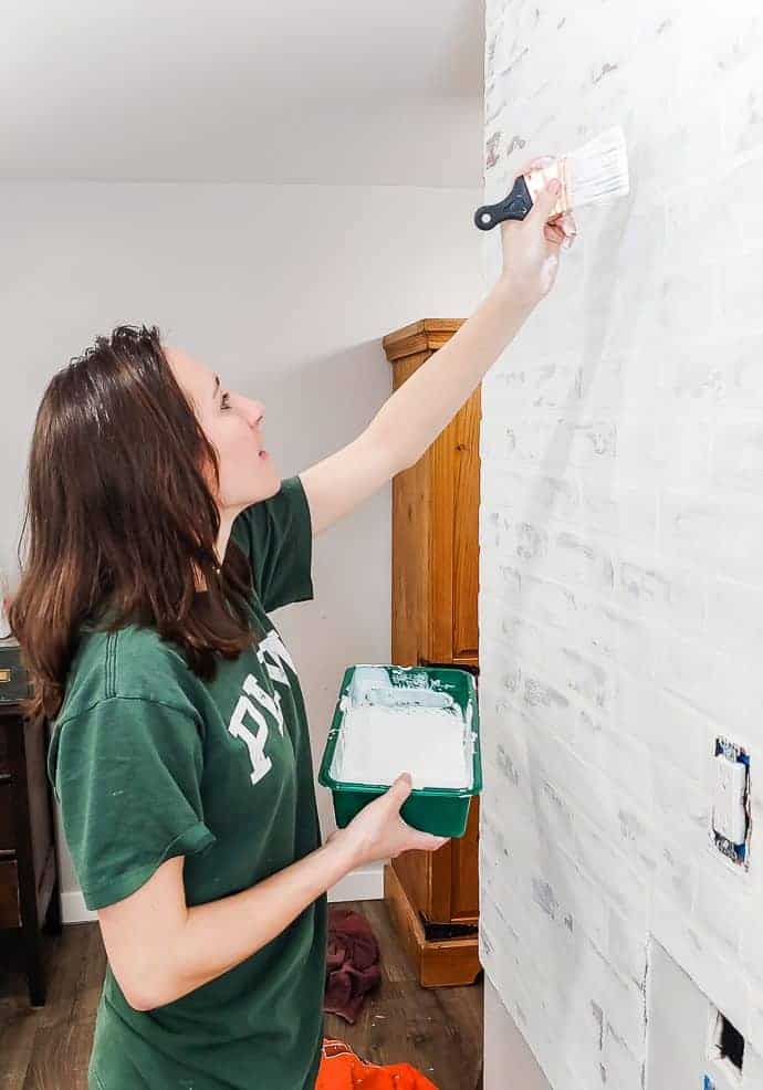 Woman painting over a faux brick wall to get a whitewashed german schmear treatment 