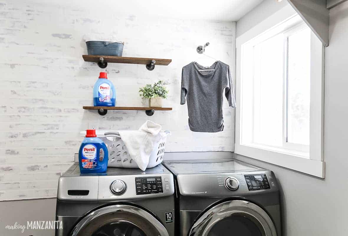 Faux brick wall in laundry room with german schmear treatment behind washer and dryer with industrial floating shelves 