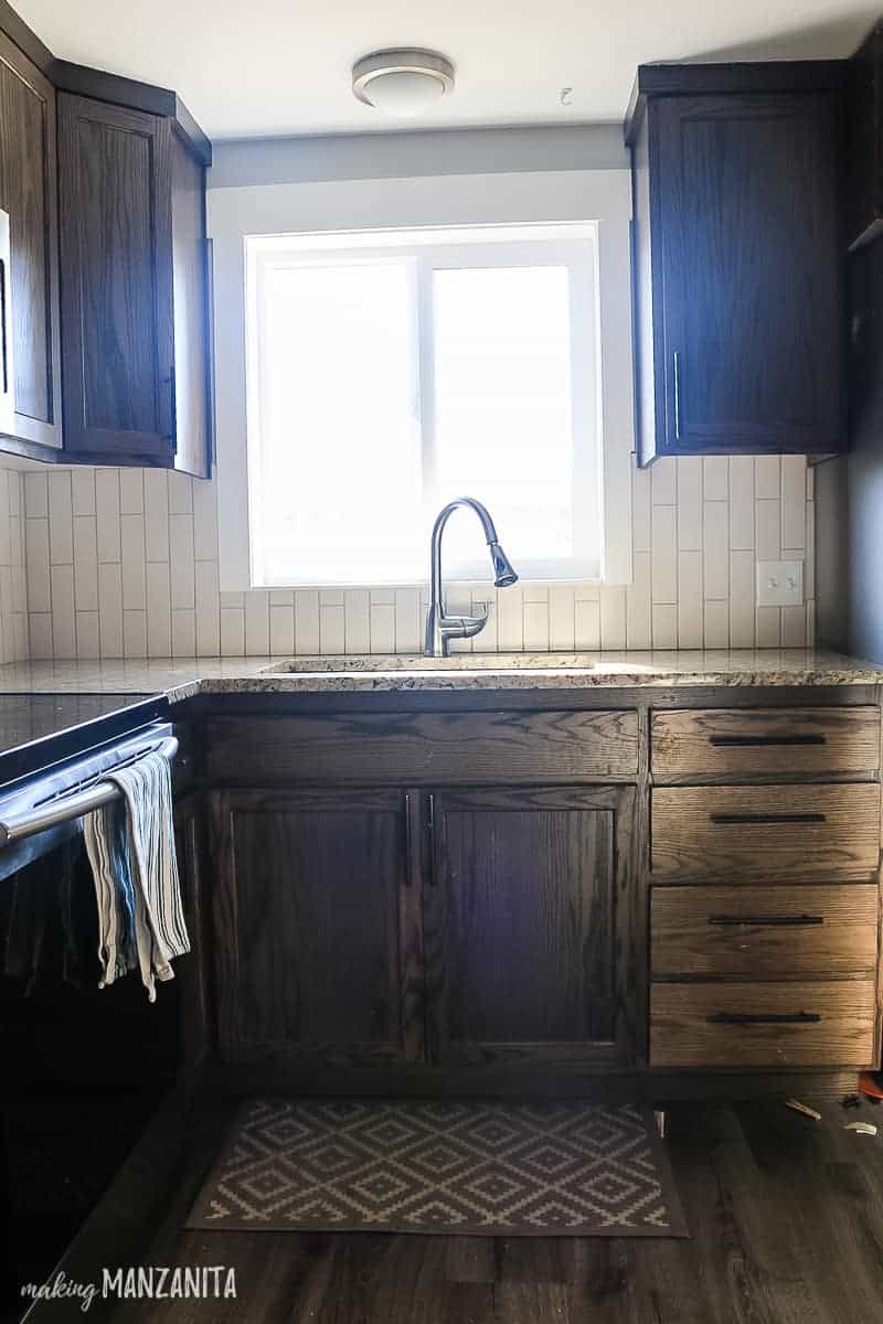 A view of the kitchen sink with dark wood cabinets and a tan tile backsplash