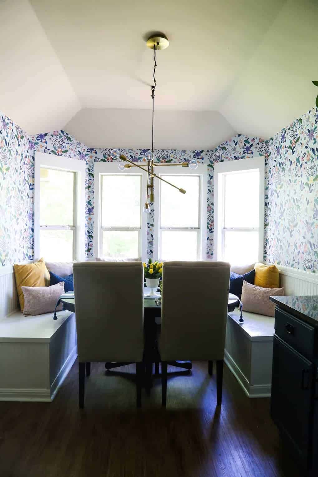 After picture with light and bright dining room with floral wallpaper, built in bench seating, modern gold light and throw pillows