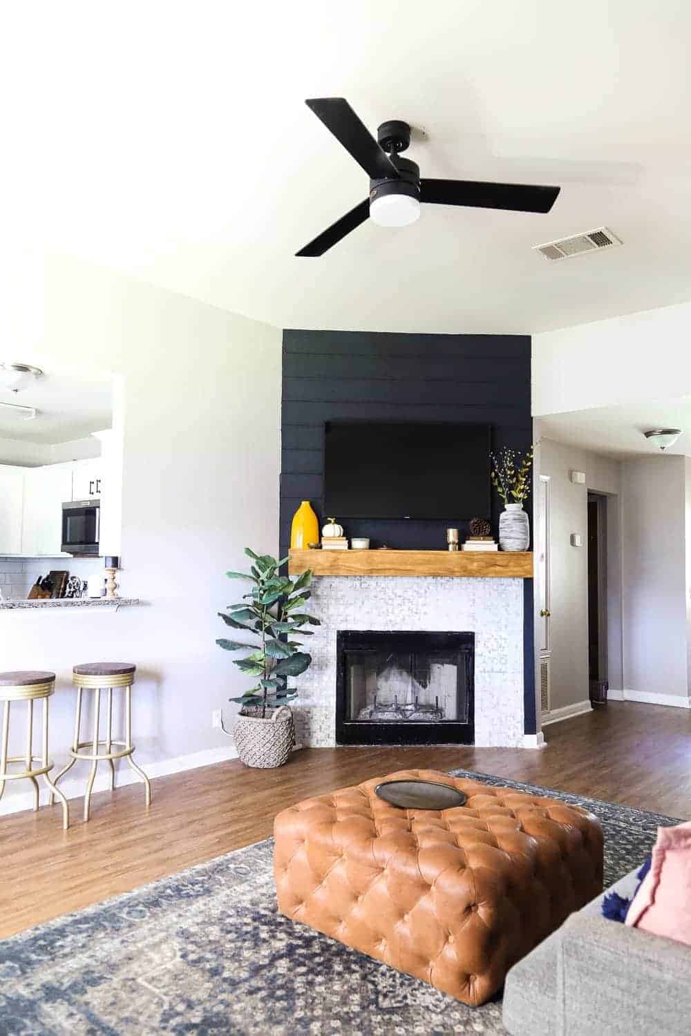 Light and bright living room with contemporary style, black shiplap fireplace, black modern ceiling fan, leather tufted ottoman 