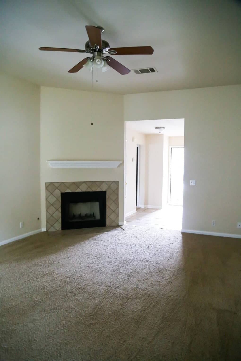 Old and dark living room with outdated tan walls, tan carpet and no furniture