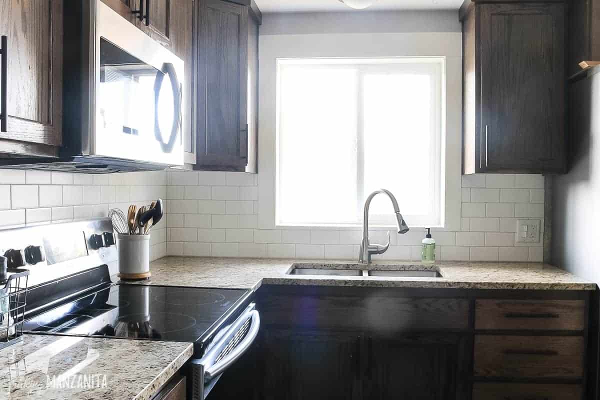 Modern farmhouse style kitchen with new subway tile backsplash, wooden cabinets, window over sink and tan granite countertops