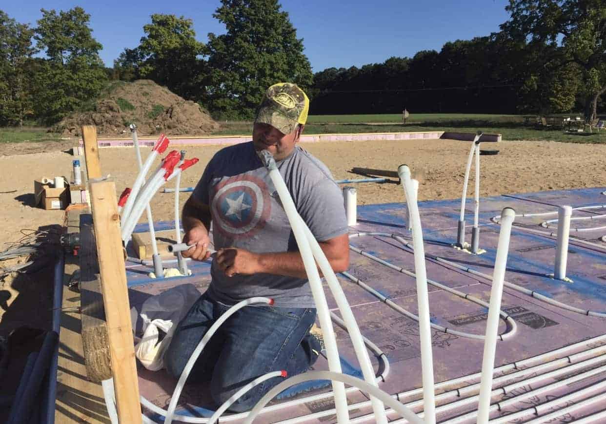 Man installing plumbing under a DIY house being built from the ground up