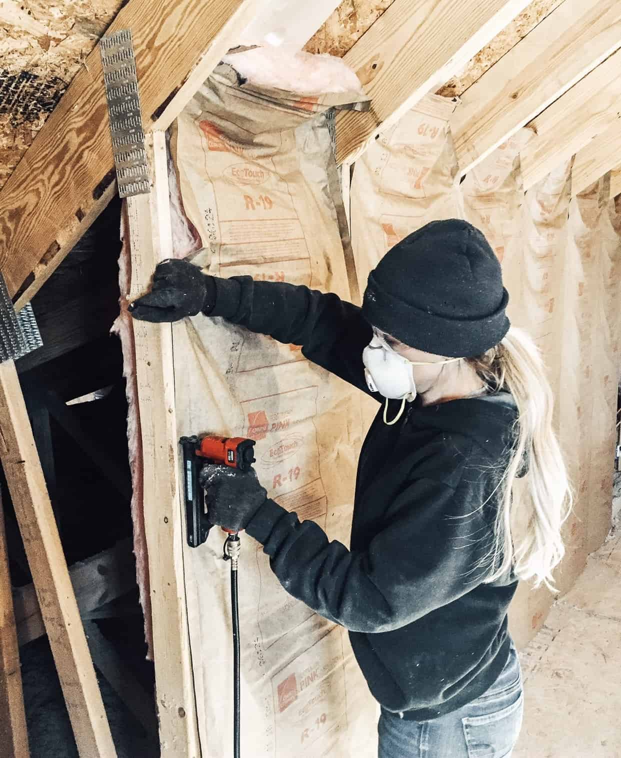 Woman installing insulation in loft area with open walls 