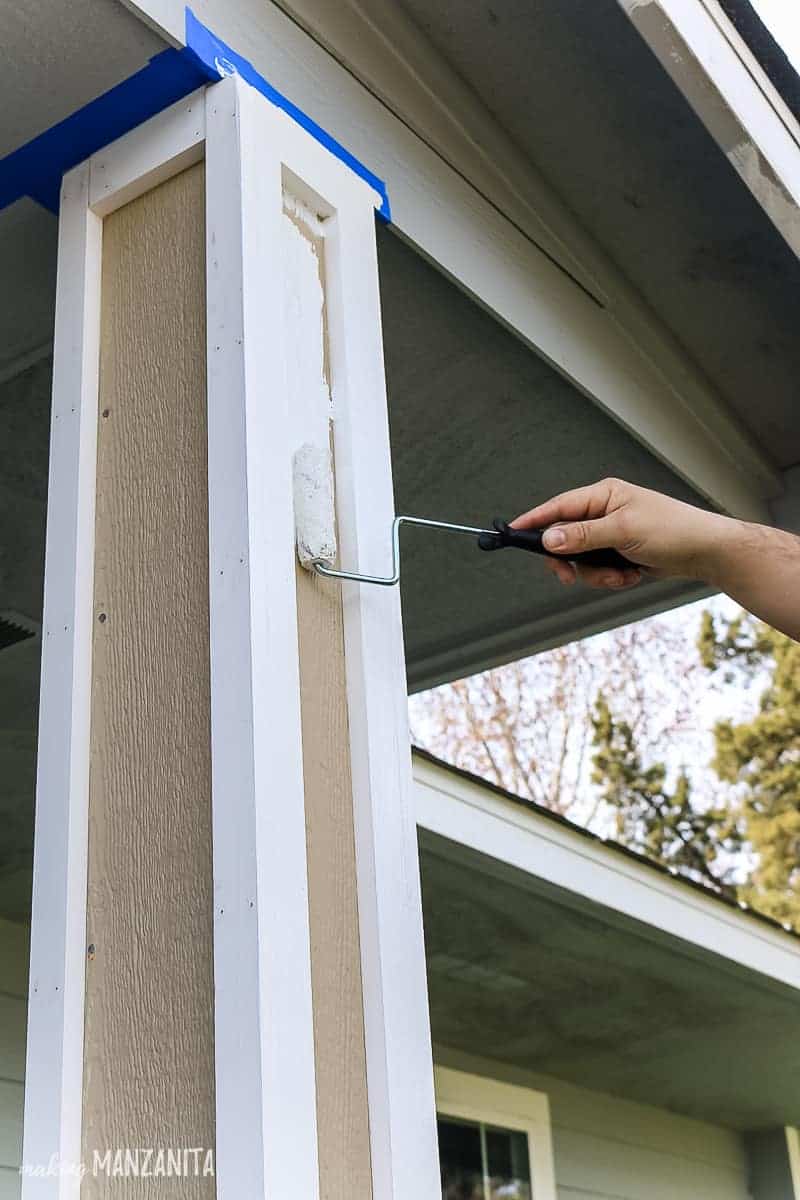 Man's hand rolling on white paint on to a new porch post with a 4 inch roller