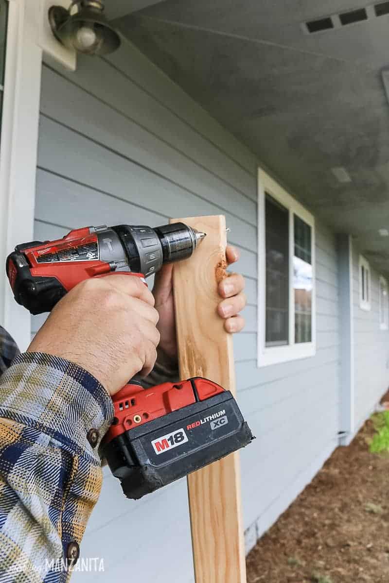 Man's hand drilling an angled pilot hole into the edge of a 2x3 