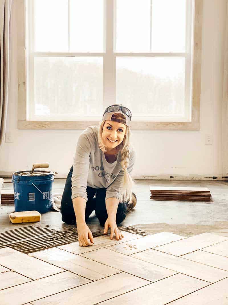 Woman tiling floor in a herringbone pattern wearing a backwards hat